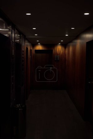Foto de Interior del pasillo oscuro vacío con paredes de madera y puertas marrones bajo techo con lámparas - Imagen libre de derechos