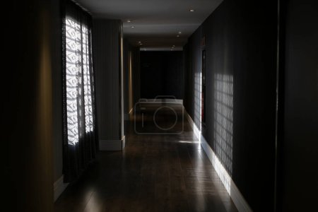 Foto de Interior de pasillo oscuro vacío con paredes grises y ventanas cortina y suelo de madera con rayos de sol - Imagen libre de derechos
