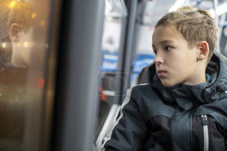 Foto de Niño adolescente mirando a través de la ventana del autobús durante su paseo nocturno por la ciudad. Niño reflexivo y aburrido quiere llegar a casa - Imagen libre de derechos