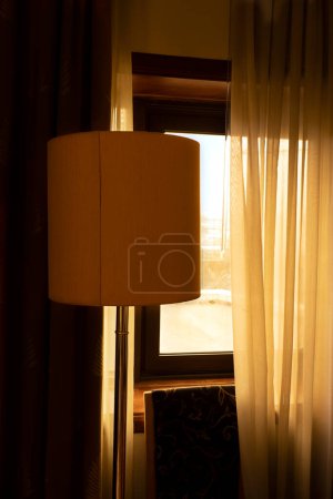 Foto de Detalles de la habitación a la luz del sol de la mañana. Lámpara de pie y silla cerca de la ventana con cortinas medio abiertas - Imagen libre de derechos