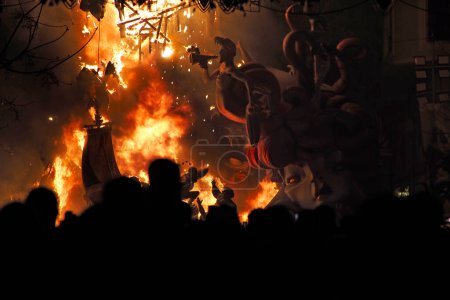 Foto de Foto horizontal de la gente viendo muñecas Ninote ardiendo en una calle iluminada por luces durante las celebraciones de Fallas en Valencia, España - Imagen libre de derechos