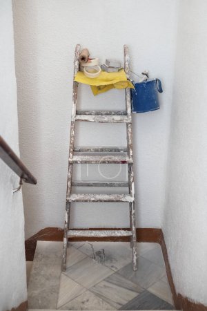 Foto de Foto vertical de un kit de reparación que consta de un cubo, un rodillo, un cepillo, cinta adhesiva y una escalera plegable en el rellano en la entrada del edificio - Imagen libre de derechos