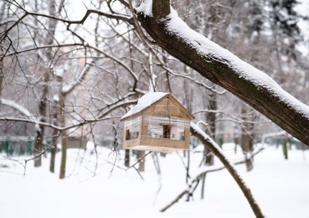 Foto de Un pajarito de madera cuelga de un árbol cubierto de nieve en un parque de invierno - Imagen libre de derechos