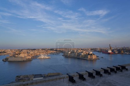 Téléchargez les photos : La Valette, Malte - 7 juin 2023 : Vue sur le Grand Port au coucher du soleil depuis Upper Barrakka Gardens jusqu'à Birgu et Senglea à Malte - en image libre de droit