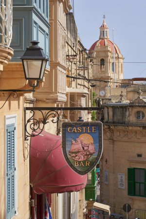 Téléchargez les photos : Victoria, Gozo, Malta - June 9, 2023: Historic buildings in Victoria on the island of Gozo in Malta.  Sign for a public house in the foreground. - en image libre de droit