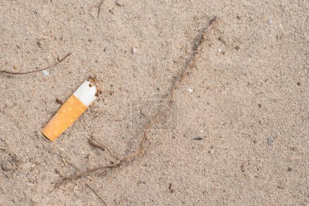 Une cigarette non allumée repose sur le sable. Espace libre pour le texte à droite.