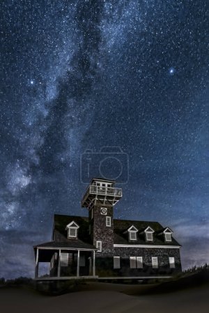 Foto de En Cape Hatteras National Seashore, en las orillas exteriores de Carolina del Norte, se encuentra la histórica Oregon Inlet Life-Saving Station construida en 1898, con la galaxia de la Vía Láctea arriba en el cielo nocturno. - Imagen libre de derechos