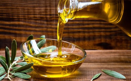 Photo for Organic olive oil pouring from carafe  into glass bowl - Royalty Free Image