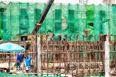 Téléchargez les photos : Bangkok, Thaïlande 5 septembre 2015 : Seau de béton hissé par une grue livrée à une équipe de travailleurs de la construction ci-dessous, pour couler du béton dans le coffrage. - en image libre de droit