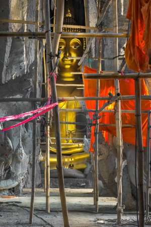 Photo for Buddha statue and an orange robe in an unfinished manmade cave with bamboo scaffolding still in place. - Royalty Free Image