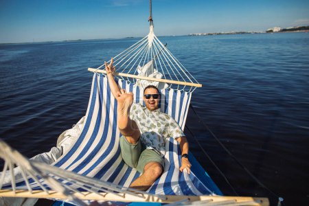 Photo for Handsome man rests in a hammock on a yacht. Leisure and fun in a water. Cool idea for rest in a water. - Royalty Free Image