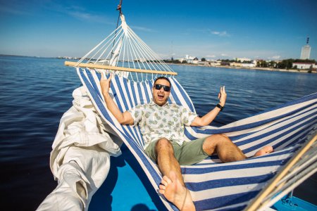Photo for Handsome man rests in a hammock on a yacht. Leisure and fun in a water. Cool idea for rest in a water. - Royalty Free Image