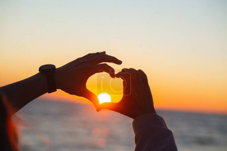 Téléchargez les photos : Mains formant une forme de coeur avec silhouette de coucher de soleil sur une mer. - en image libre de droit