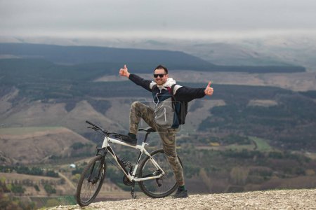 Téléchargez les photos : Un homme heureux a gravi la montagne à vélo et se réjouit de la victoire - en image libre de droit