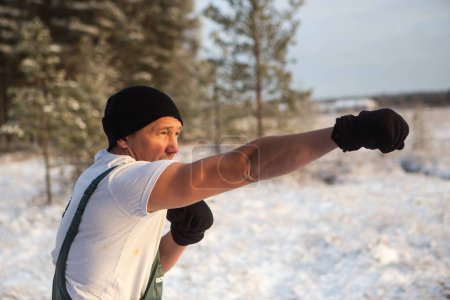 Foto de Joven en una camiseta hombre con aspecto atlético en el bosque de invierno rodeado de copos de nieve. Concepto de aclimatación deportiva y fría. Foto de alta calidad - Imagen libre de derechos