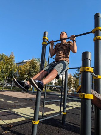 Foto de Un hombre normal haciendo ejercicio afuera. Manteniendo su parte superior del cuerpo por encima de la barra horizontal. Gente real. - Imagen libre de derechos