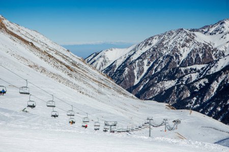 Skilifte, Skifahrer und Snowboarder auf Pisten in wunderschöner Winterlandschaft mit Bergkette im Hintergrund, Kasachstan, Shymbulak