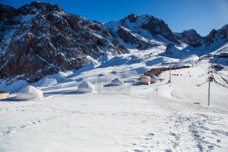 Shymbulak mountain resorts ski slopee with eco hotel, yurts, skiers and snowboarders. Skiers at slopes of ski resort Shymbulak.