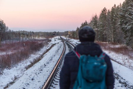 Photo for Male hiker with backpack going on a railroad in a winter dusk - Royalty Free Image