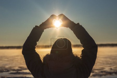 Foto de Mujer haciendo el corazón con las manos al aire libre en una puesta de sol helada, primer plano. Solsticio de invierno. Foto de alta calidad - Imagen libre de derechos