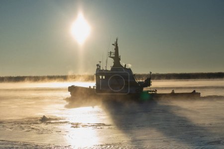 Téléchargez les photos : Le remorqueur brise la glace près du rivage dans une rivière gelée et brumeuse. Photo de haute qualité - en image libre de droit