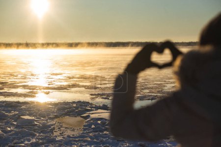 Photo for Woman making heart with hands outdoors in a frosty sunset, closeup. Focus on ice floes. High quality photo - Royalty Free Image