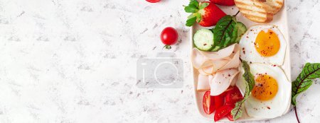Photo for Fried eggs with ham, tomatoes, cucumber, strawberries and toasts. Delicious English Breakfast. Brunch. Top view, banner - Royalty Free Image