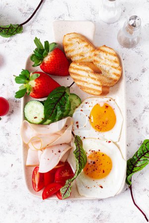 Téléchargez les photos : Fried eggs with ham, tomatoes, cucumber, strawberries and toasts. Delicious English Breakfast. Brunch. Top view, overhead - en image libre de droit