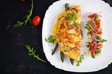 Téléchargez les photos : Keto breakfast. Omelette with cheese, red onion and asparagus on dark table. Italian frittata. Keto, ketogenic lunch. Top view, overhead, copy space - en image libre de droit
