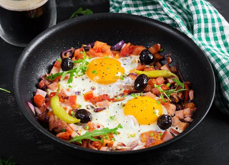 Foto de Fried eggs with vegetables on pan - pepperoni, tomatoes, ham, onion and black olives. Ketogenic breakfast. - Imagen libre de derechos