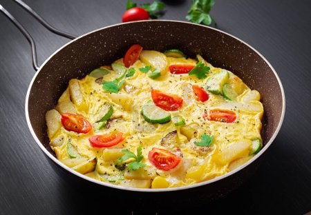 Foto de Omelette with tomatoes,  zucchini and potatoes on dark background. Healthy diet food for breakfast. Tasty morning food. - Imagen libre de derechos