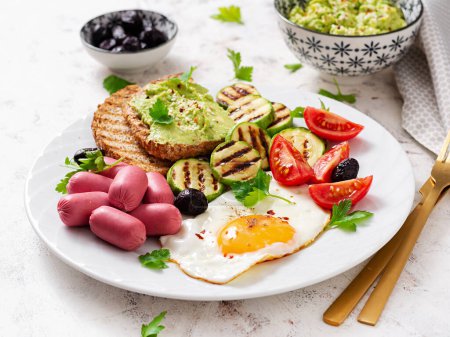 Photo for Fried egg with mini sausage, tomatoes, grilled zucchini, black olives and toasts with guacamole. English Breakfast. Brunch. - Royalty Free Image
