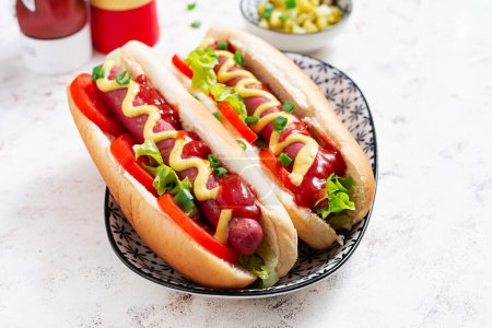 Téléchargez les photos : Hot dog avec saucisse grillée, tomate et laitue sur fond clair. Hot dog américain. - en image libre de droit
