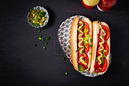 Photo for Hot dog with grilled sausage, tomato and lettuce on dark background. American hotdog. Top view, overhead - Royalty Free Image