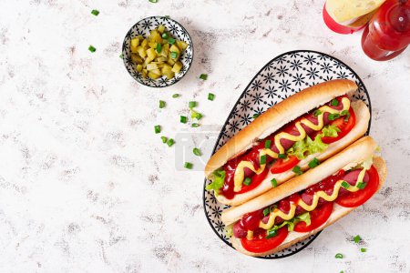 Foto de Hot dog with grilled sausage, tomato and lettuce on light background. American hot dog. Top view, overhead - Imagen libre de derechos