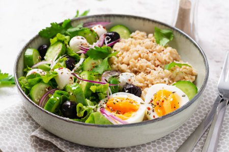 Breakfast oatmeal porridge with boiled eggs, cucumber, mozzarella cheese and green herbs. Healthy balanced food.