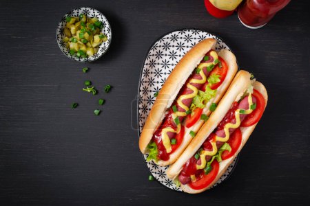 Photo for Hot dog with grilled sausage, tomato and lettuce on dark background. American hotdog. Top view, overhead - Royalty Free Image