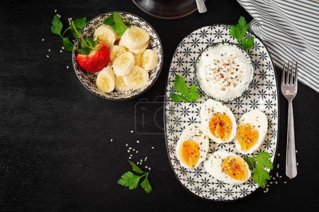 Photo for Boiled eggs with yogurt, peppers, parsley and  banana dessert. Healthy diet food for breakfast. Top view, flat lay. - Royalty Free Image