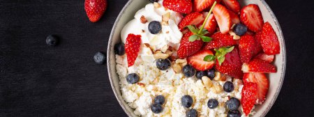 Foto de Cottage cheese, curd cheese with fresh strawberries, blueberries, nuts and yogurt in a bowl.  Healthy dairy product rich in calcium and protein. Top view, banner - Imagen libre de derechos