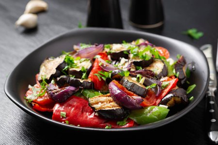 Téléchargez les photos : Légumes grillés aubergine, poivron, courgettes, oignon rouge, tomate à l'ail sur une assiette noire. - en image libre de droit
