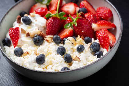 Téléchargez les photos : Cottage cheese, curd cheese with fresh strawberries, blueberries, nuts and yogurt in a bowl.  Healthy dairy product rich in calcium and protein. - en image libre de droit