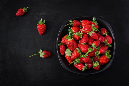 Photo for Strawberries in a black plate on dark background. Top view, above - Royalty Free Image