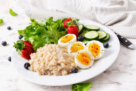 Photo for Breakfast oatmeal porridge with boiled eggs, cucumber and strawberry. Healthy balanced food. - Royalty Free Image
