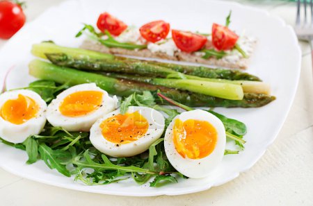 Photo for Green asparagus with boiled eggs and sandwich cream cheese on a white plate. - Royalty Free Image
