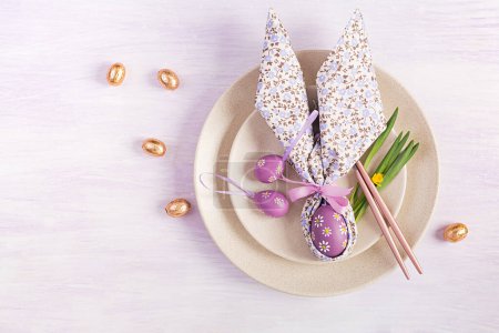 Photo for Easter table setting. White plate with a napkin folded in the shape of a rabbit, Easter and chocolate eggs on a pink background. Happy Easter holiday concept. Top view, flat lay - Royalty Free Image