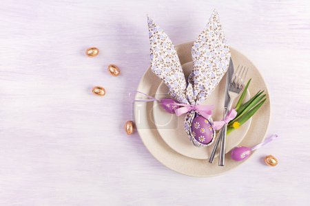 Téléchargez les photos : Table de Pâques. Assiette blanche avec une serviette pliée en forme de lapin, oeufs de Pâques et chocolat sur un fond rose. Joyeux Noël concept de vacances. Vue de dessus, plan plat - en image libre de droit