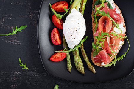 Photo for Keto breakfast. Fried asparagus with poached egg and toast with prosciutto or jamon. Ketogenic diet. Healthy food. Top view, flat lay - Royalty Free Image
