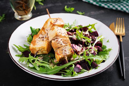 Téléchargez les photos : Brochettes de tofu cuites au four en sauce et salade de betteraves, roquette avec sauce au yaourt aux légumes. Concept de nourriture végétalienne saine. Aliments sains. - en image libre de droit