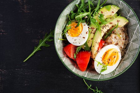 Photo for Breakfast oatmeal porridge with boiled eggs, avocado, tomatoes and green herbs. Healthy balanced food. Top view, flat lay - Royalty Free Image