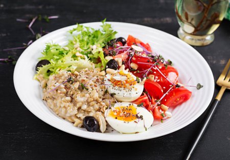 Photo for Breakfast oatmeal porridge with boiled egg, cherry tomatoes, olives, nuts and microgreens. Healthy balanced food. - Royalty Free Image